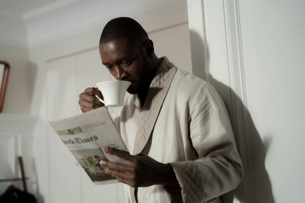 a Black man reading positive black news in the newspaper while drinking coffee